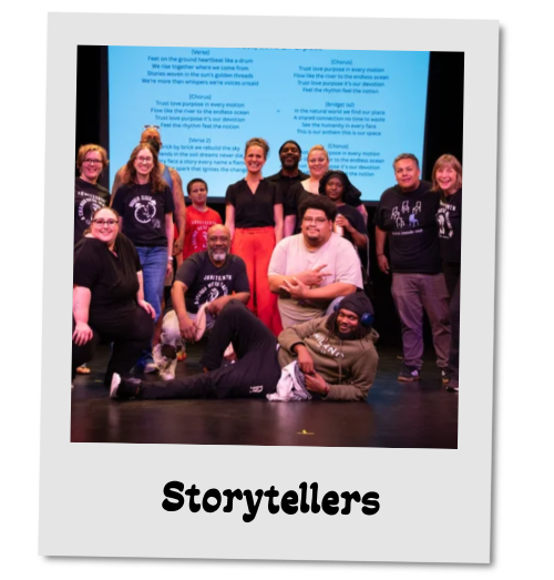 Photo styled as a tilted polaroid labeled "Storytellers." A group poses together on a stage in front of a screen projecting text, several wearing matching printed t-shirts.